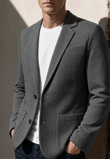 Mann trägt grauen Blazer und weißes T-Shirt, Hände in den Taschen
