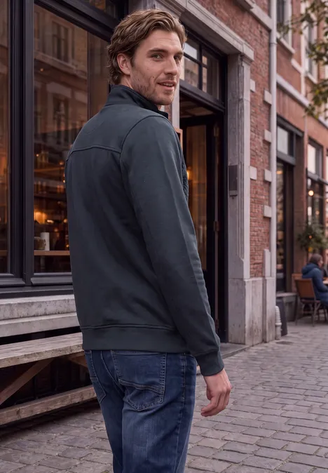 Un homme en jean et veste marche sur une rue pavée devant un café et regarde par-dessus son épaule.
