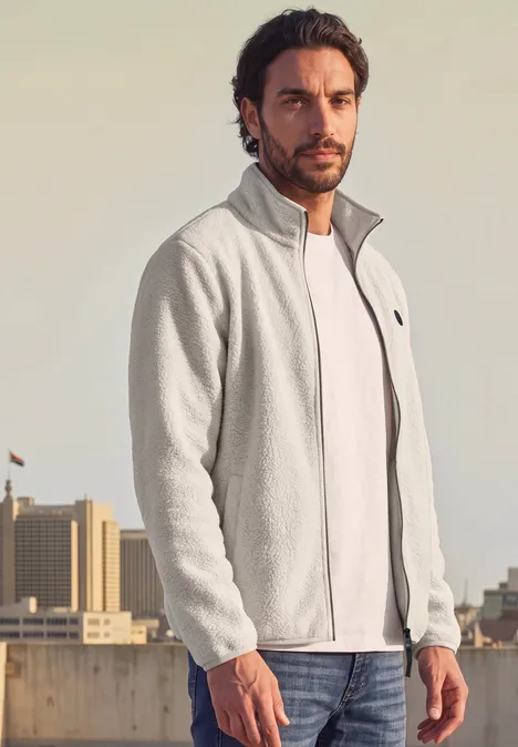 Veste en peluche avec col montant et fermeture à zip classic beige Un homme porte une veste polaire grise sur un t-shirt blanc, debout sur un toit urbain.