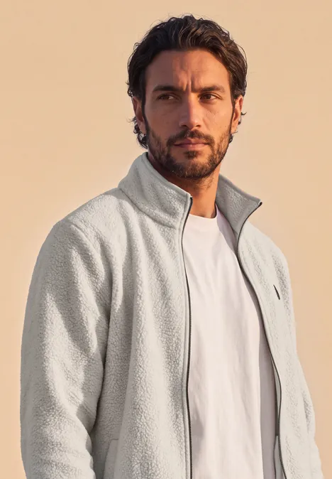 Veste en peluche avec col montant et fermeture à zip classic beige Un homme aux cheveux foncés et barbe porte une veste polaire grise et un T-shirt blanc devant un fond clair.