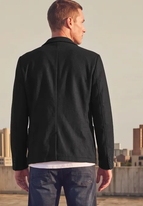 Un homme de dos porte une veste noire et regarde le panorama urbain.