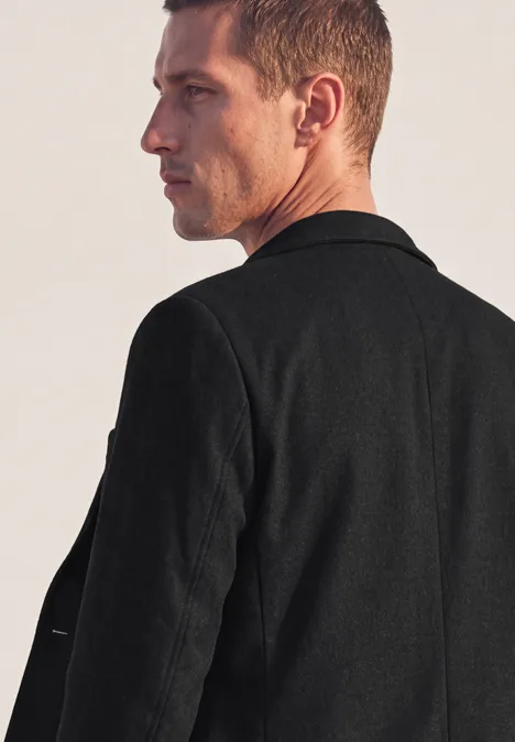 Profil latéral d’un homme aux cheveux courts portant une veste noire, regard tourné vers la droite.