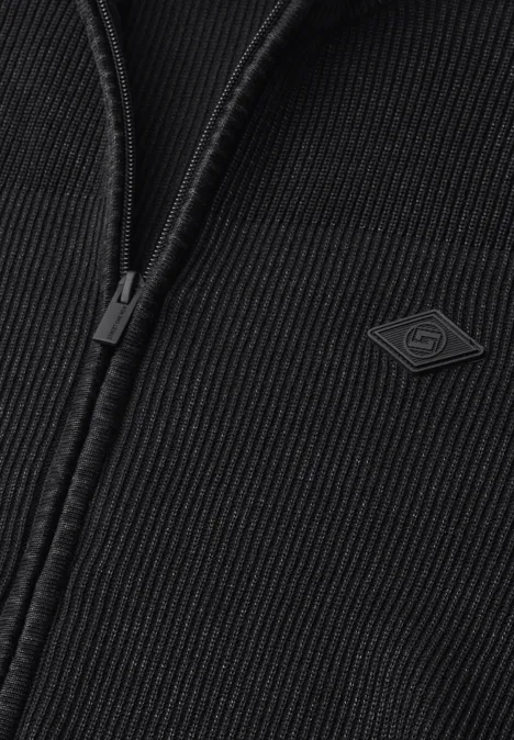 Vest met opstaande kraag en een mix van texturen Black Close-up van een zwarte ribgebreide jas met ritssluiting en klein logo-label.