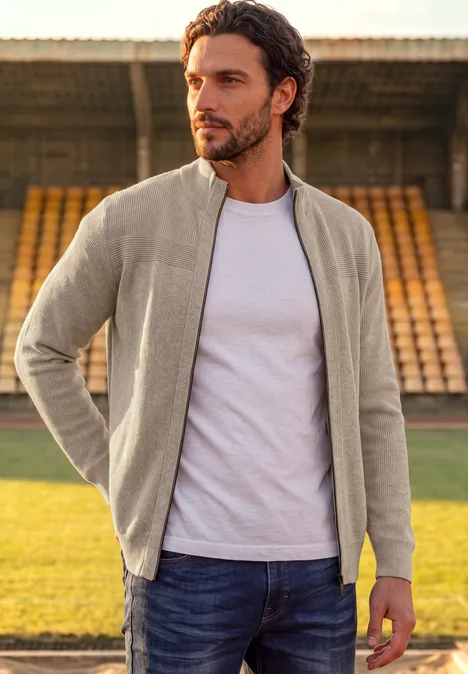 Ottoman Jacke mit Rippstruktur antique beige Ein Mann in grauer Jacke, weißem T-Shirt und Jeans steht auf einem Sportplatz vor leeren Tribünen.