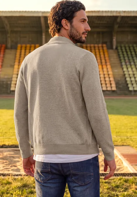 Ottoman Jacke mit Rippstruktur antique beige Mann im beigen Pullover und Jeans steht mit dem Rücken zum Betrachter auf einer Laufbahn vor leeren Stadionrängen