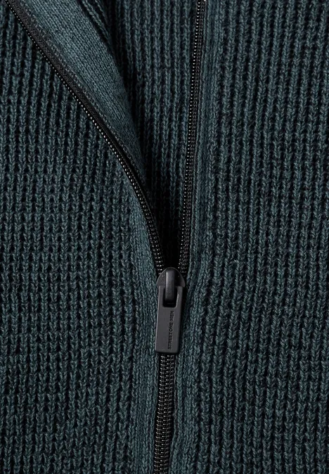Gros plan sur un pull en maille côtelée vert foncé avec fermeture éclair.