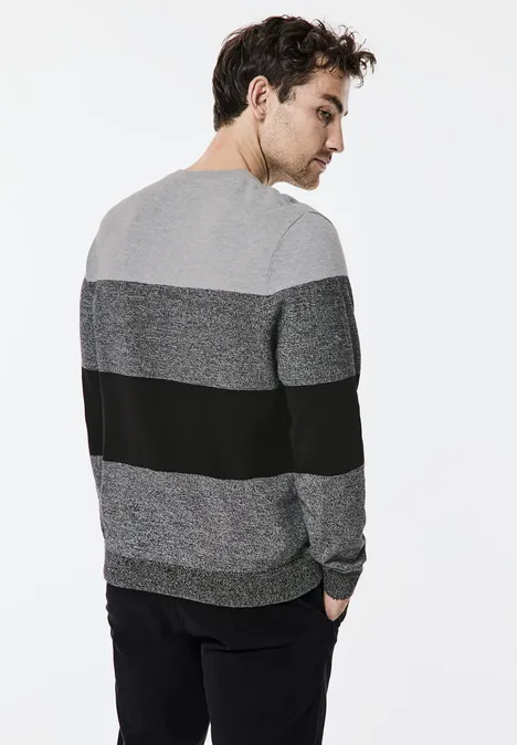Homme portant un pull gris et noir, vu de dos, tourne la tête.