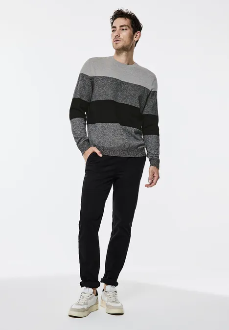 Homme en pull rayé, pantalon noir et baskets blanches sur fond blanc.
