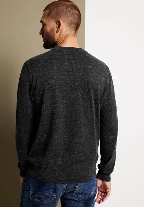 Homme vu de dos en pull sombre et jean devant un mur bicolore.