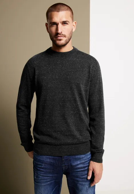 Homme en pull foncé et jean devant un fond bicolore.