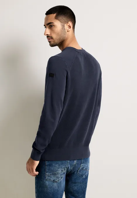 Homme en pull bleu foncé et jean, vu de dos, regarde sur le côté.