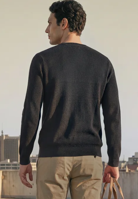 Trui met ronde hals en gemengde texturen Black Een man op een dak gezien van achteren, draagt een donkere trui, lichte broek en houdt een tas vast.
