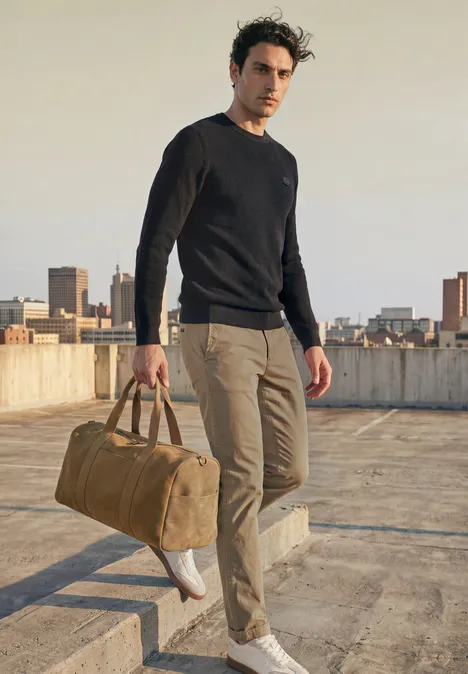 Trui met ronde hals en gemengde texturen Black Een man loopt op een dak met een reistas, gekleed in een zwarte trui en een beige broek.