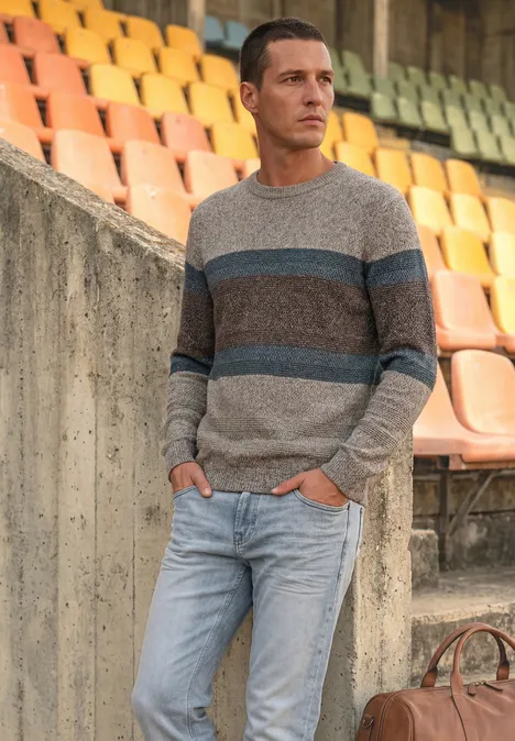 Trui met ronde hals en streepjespatroon bright beige melange Een man leunt tegen stadiontribune, draagt gestreepte trui, spijkerbroek en een bruine tas.