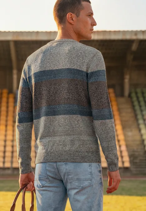 Trui met ronde hals en streepjespatroon bright beige melange Een man in een gestreepte trui en spijkerbroek staat achteraan op een sportveld voor lege tribunes.