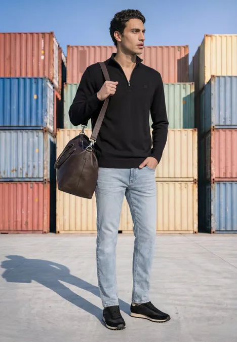Basic Pullover mit Troyerkragen Black Ein Mann in schwarzem Polo, hellen Jeans und Leder-Tasche posiert vor bunten Frachtcontainern.
