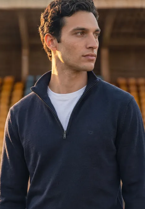 Basic Pullover mit Troyerkragen dark basic blue Junger Mann in dunkelblauem Pullover mit halbem Reißverschluss und weißem T-Shirt vor unscharfem Hintergrund.