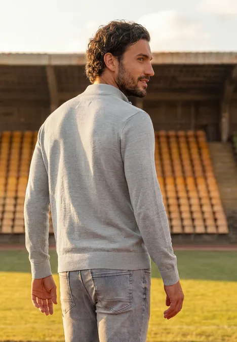 Ein Mann in grauem Pullover und Jeans steht auf dem Fußballfeld und blickt über die Schulter zurück.