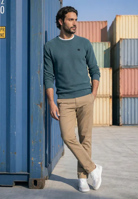 Trui met ronde hals en schouderdetail cold blue Een man leunt nonchalant tegen een blauwe container, omringd door kleurrijke containers.
