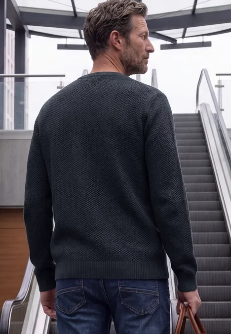 Ein Mann in schwarzem Pullover trägt eine Tasche und steht auf einer Rolltreppe.