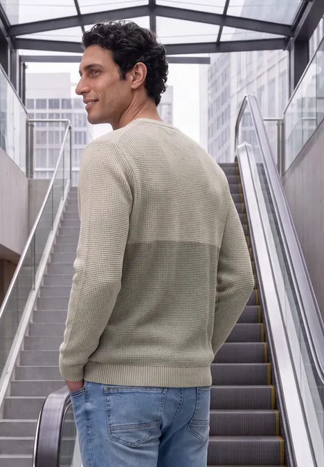 Ein Mann in hellem Pullover steht auf einer Rolltreppe im modernen Gebäude und blickt lässig über die Schulter.
