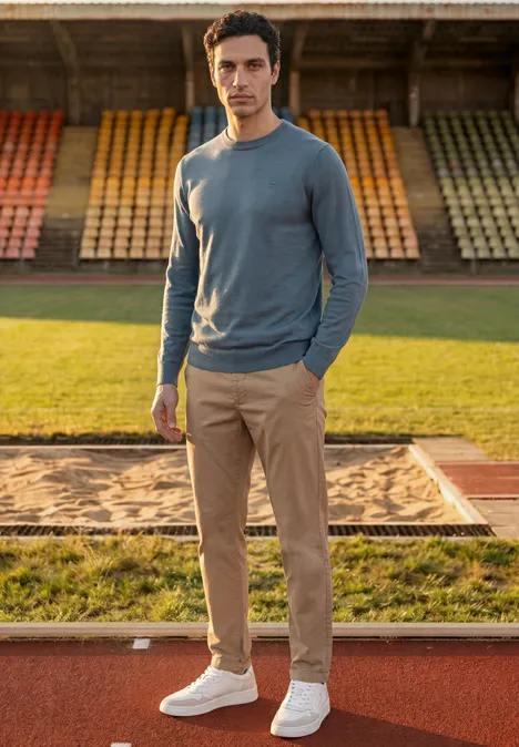 Eenvoudige trui met ronde hals in effen kleur cold blue Een man in een grijze trui en beige broek staat op de atletenbaan voor lege tribunes.