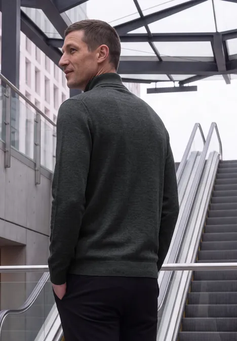 Ein Mann in grauem Pullover steht vor einer Rolltreppe in moderner Architektur.