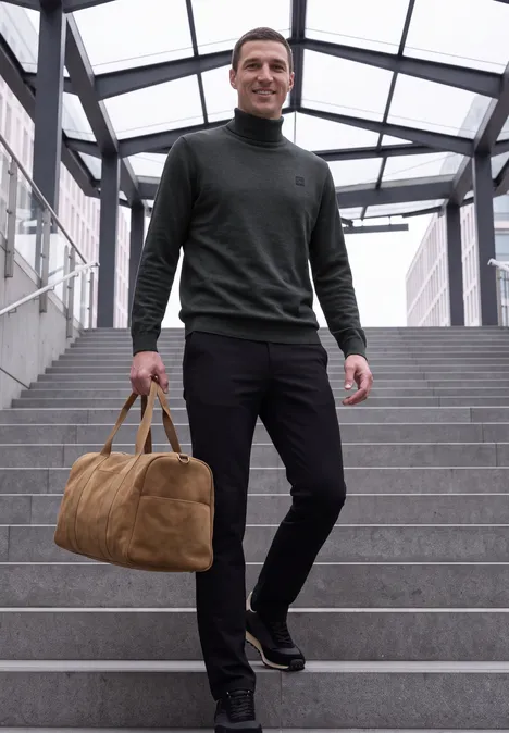 Ein Mann trägt eine braune Reisetasche, lächelt und geht eine Treppe in einem modernen Glasgang hinunter.