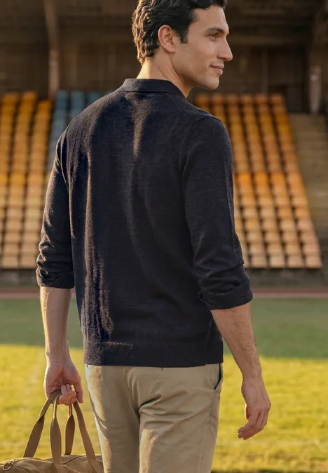 Strick Poloshirt im Mouliné Look dark ink blue Ein Mann in Pullover und Chinos trägt eine Tasche und geht an leeren Tribünen vorbei