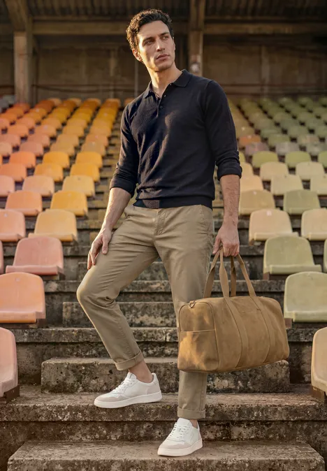 Strick Poloshirt im Mouliné Look dark ink blue Ein Mann steht auf Stadionstufen, trägt lässige Kleidung und hält eine beige Reisetasche.