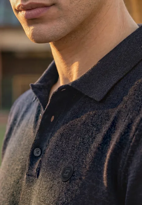 Strick Poloshirt im Mouliné Look dark ink blue Nahaufnahme eines Mannes, der ein dunkelblaues Poloshirt mit offenem Kragen und dezentem Logo trägt.