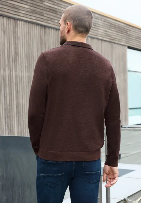 Gebreid poloshirt in mouliné-look maroon brown Een man in een bruine trui en spijkerbroek staat voor een modern gebouw met houtbekleding.