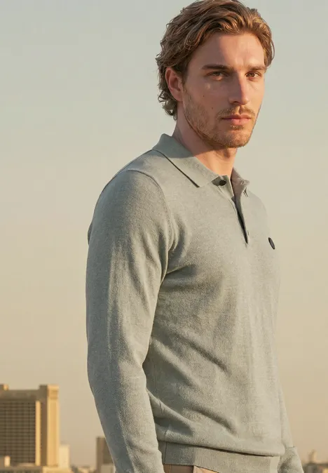 Gebreid poloshirt in mouliné-look willow green Een man met bruin haar draagt een grijze polo met lange mouwen en staat voor een stadsgezicht.