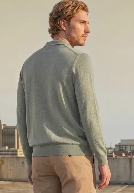 Gebreid poloshirt in mouliné-look willow green Een man in een grijze trui en beige broek staat op een dak en kijkt over de stad.