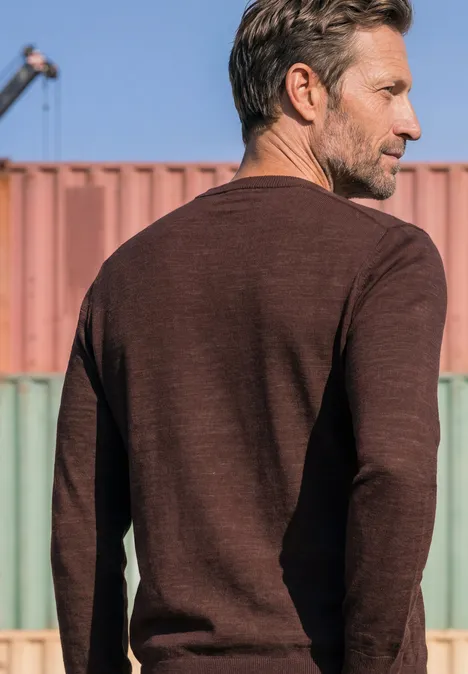 Trui met ronde hals van puur katoen maroon brown Een man in een bruin shirt met lange mouwen gezien van achter, voor kleurrijke zeecontainers.