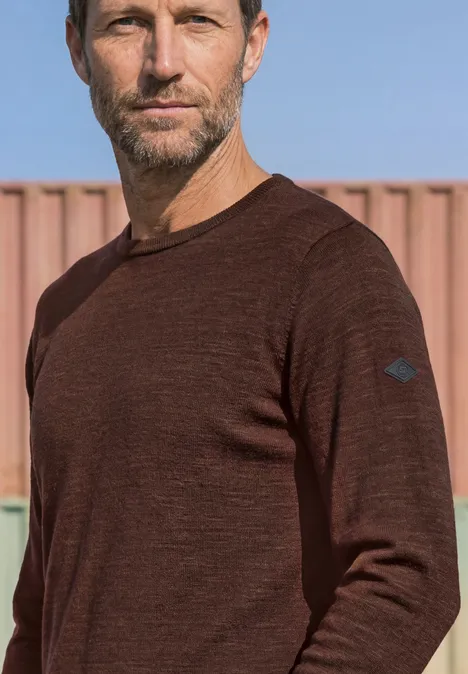 Trui met ronde hals van puur katoen maroon brown Een man met kort haar en baard draagt een bruin shirt met lange mouwen voor een containerachtergrond.