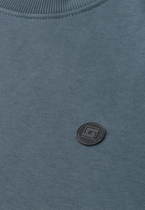 Gros plan sur un sweat-shirt bleu avec un patch rond noir près du col.