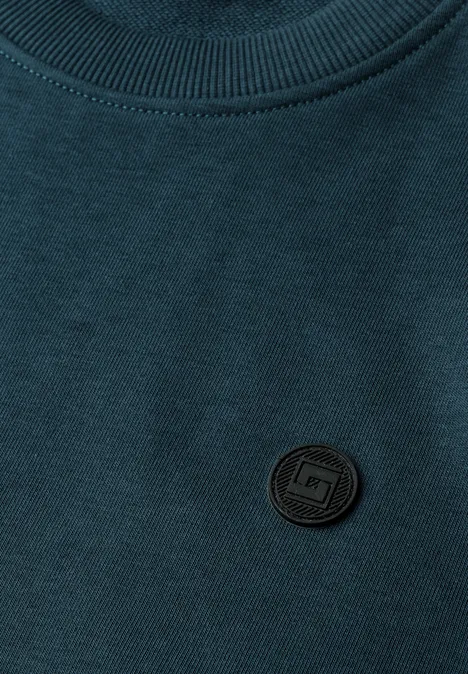 T-shirt vert foncé avec un écusson logo noir rond sur la poitrine.
