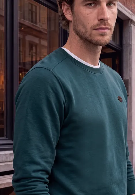 Un homme en sweat-shirt vert pose devant un bâtiment ancien.