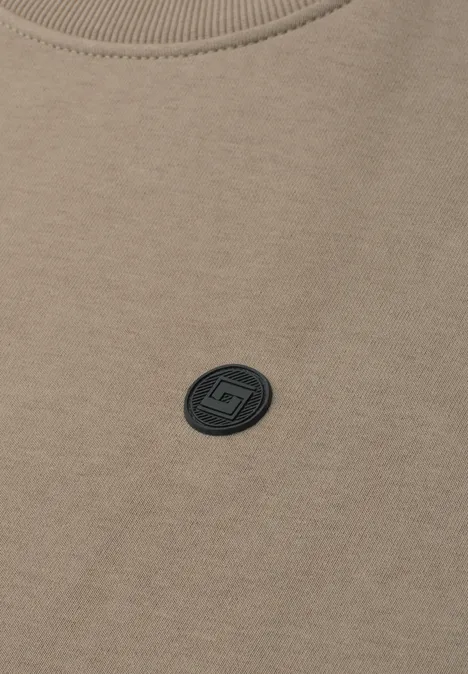 Sweat beige à col rond avec petit écusson logo noir sur la poitrine.