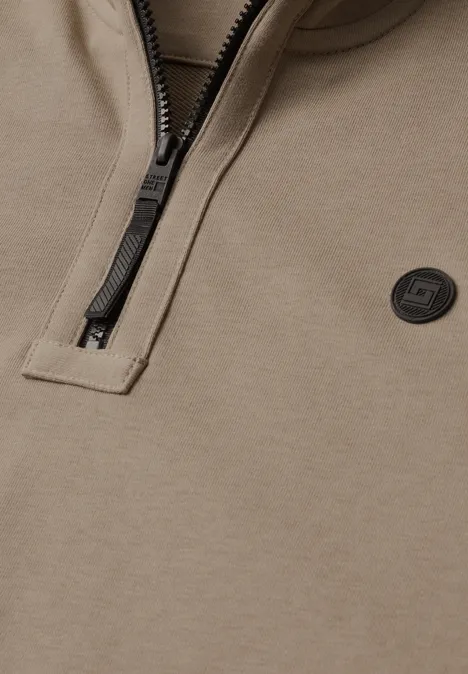 Nahaufnahme eines taupefarbenen Half-Zip-Sweatshirts mit schwarzem Reißverschluss und rundem Logo.