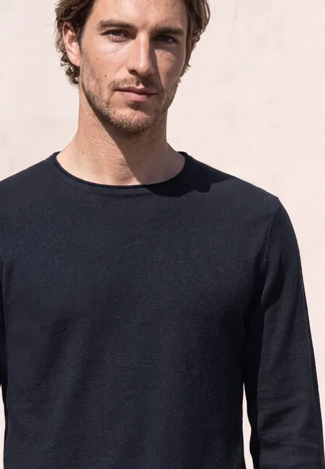 Ein Mann mit braunen Haaren und dunklem Pullover vor hellem Hintergrund.