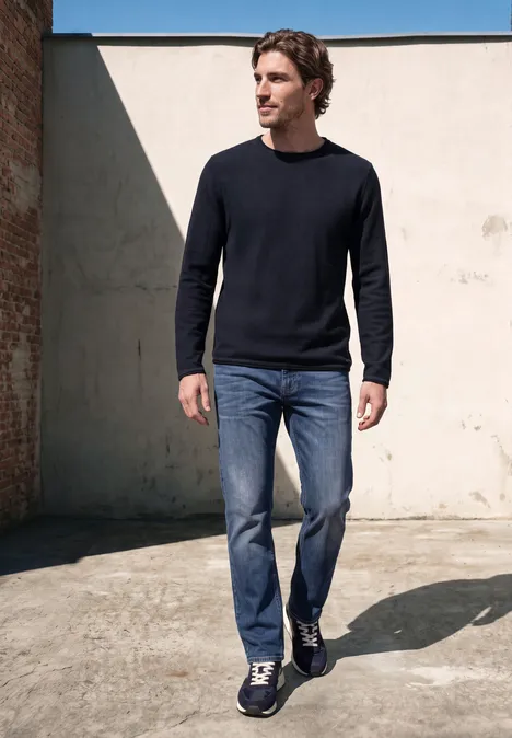 Ein Mann in Jeans und dunklem Pullover geht vor einer Mauer.