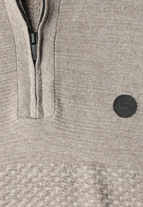 Nahaufnahme eines beigen Strickpullovers mit Reißverschluss und rundem Logo-Patch.