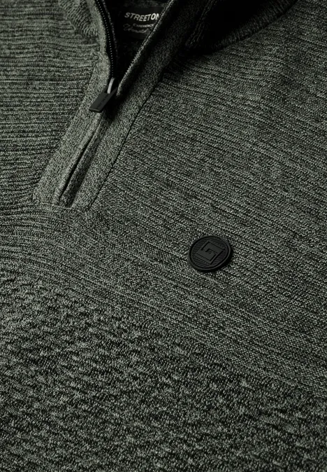 Nahaufnahme eines grauen Strickpullovers mit Reißverschluss und rundem Logo-Emblem