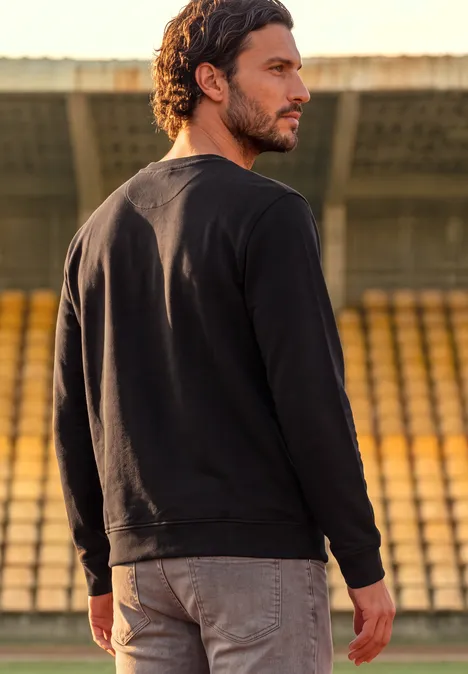 Ein Mann im schwarzen Pullover steht auf einer Tribüne und blickt in die Ferne.