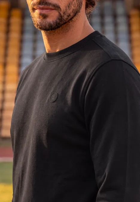 Ein Mann in schwarzem Langarmshirt vor Stadiontribüne.