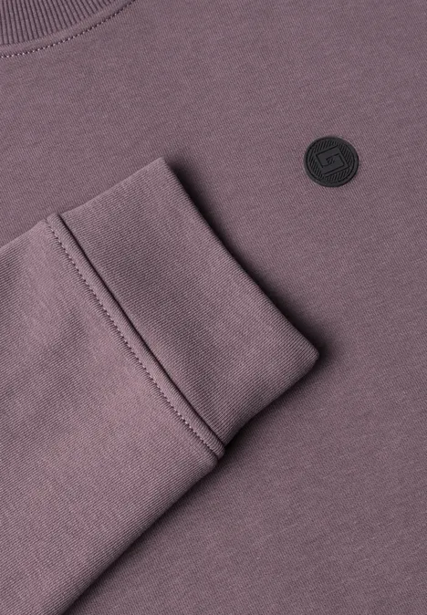 Fliederfarbenes Sweatshirt mit gefaltetem Ärmelbündchen und rundem schwarzem Logo.