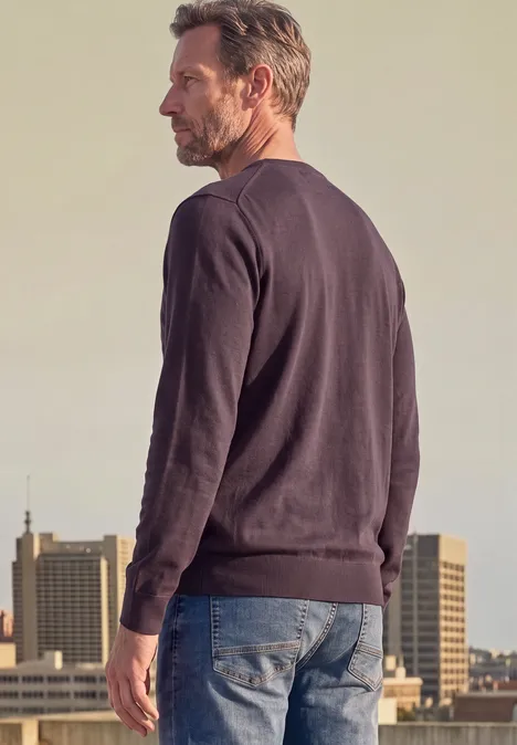 Ein Mann steht in Jeans und Pullover mit dem Rücken zur Kamera vor städtischer Kulisse.