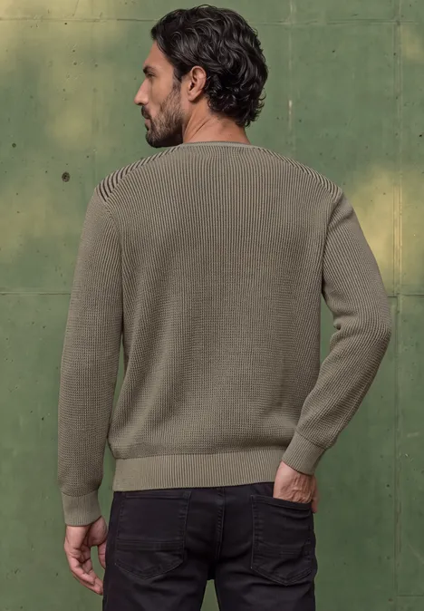 Ein Mann steht von hinten in einem khakifarbenen Pullover vor grünem Hintergrund.